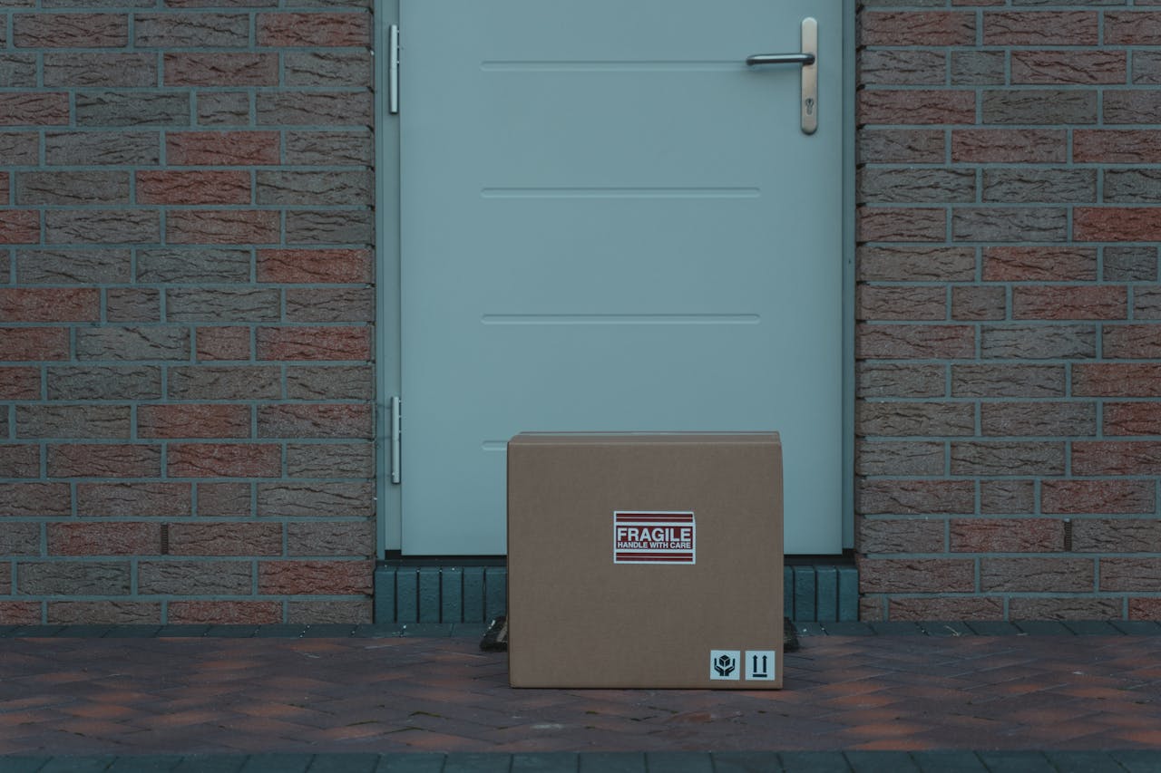 why-choose-us-02 Cardboard box placed outside a brick-walled entrance, labeled fragile for delivery.